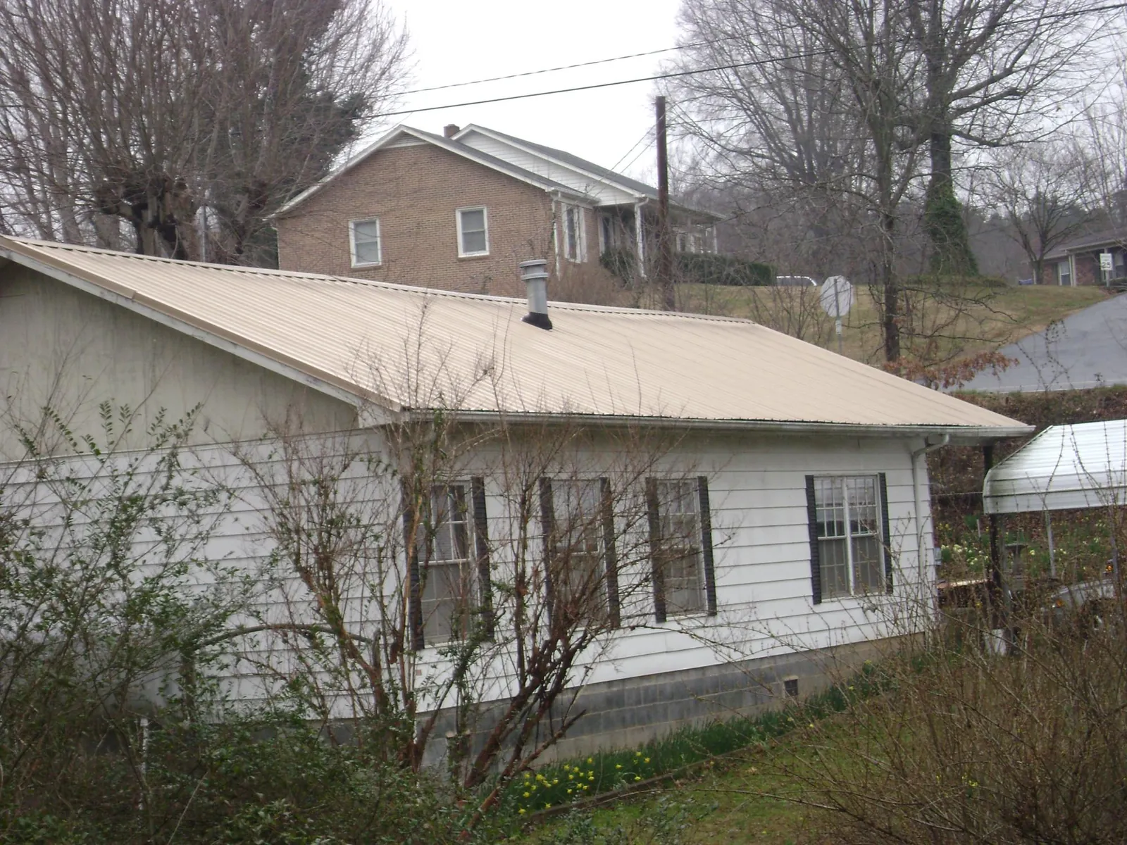 Tan metal roof on a white sided house set into a hillside — Commercial Roofing by Roofing Brothers in Liberty Center